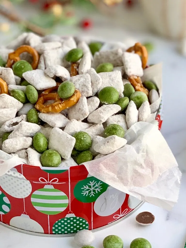 A colorful tin of puppy chow, pretzels, and white and green peppermint candies.