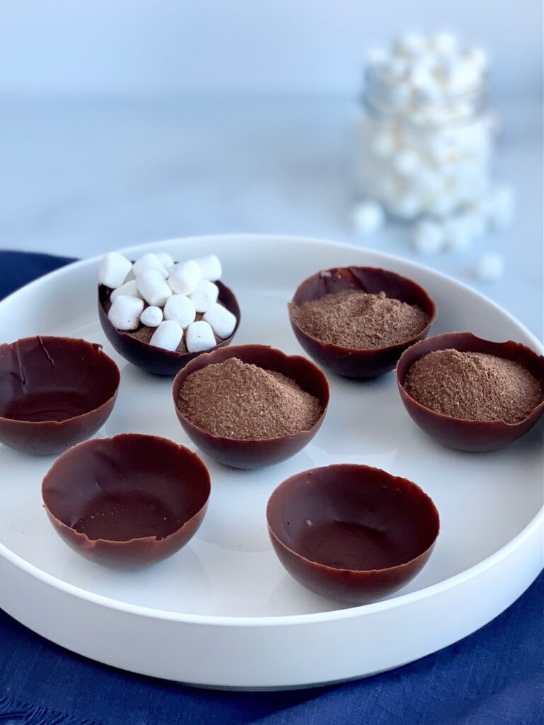 A platter full of 7 chocolate wells. Half of the chocolate wells are filled with hot chocolate mix. The other 3 are empty.