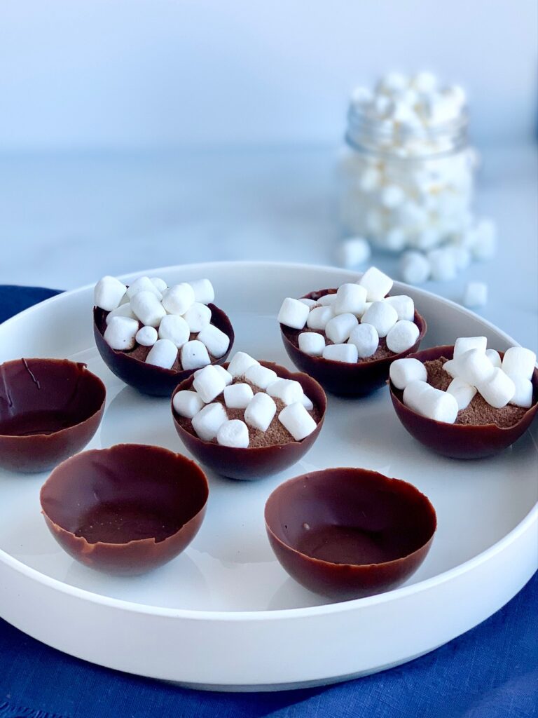 A platter full of 7 chocolate wells. Half of the chocolate wells are filled with hot chocolate mix and mini marshmallows. The other 3 are empty.