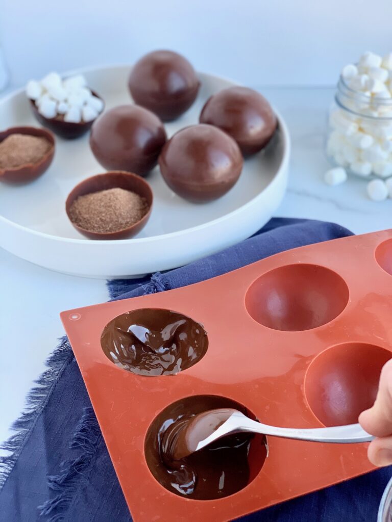 A red silicon mold of wells. There is melted chocolate in the wells that will eventually form a thin chocolate well.