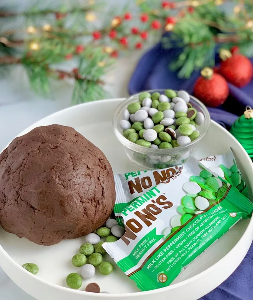 A large chocolate dough ball on a serving platter with a bowl of No Whey Food's Peppermint No No's (white and green peppermint candies)