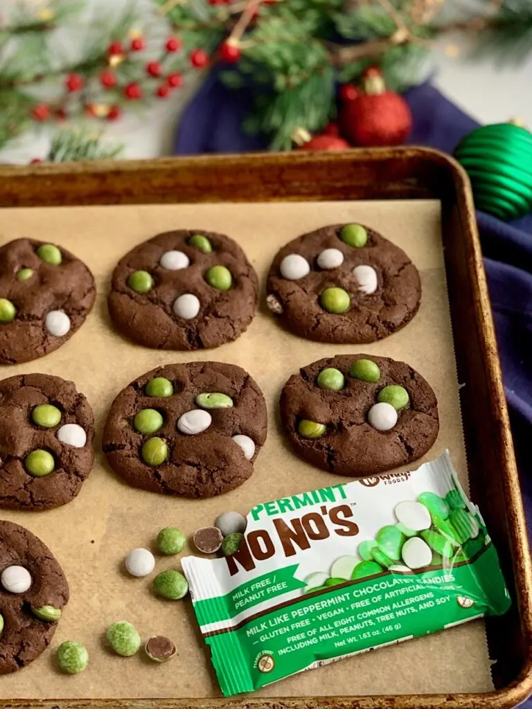 A baking sheet of baked chocolate cookies with green and white peppermint candies on top.