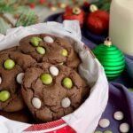 A festive red holiday tin filled with chocolate cookies featuring green and white candies on the top.