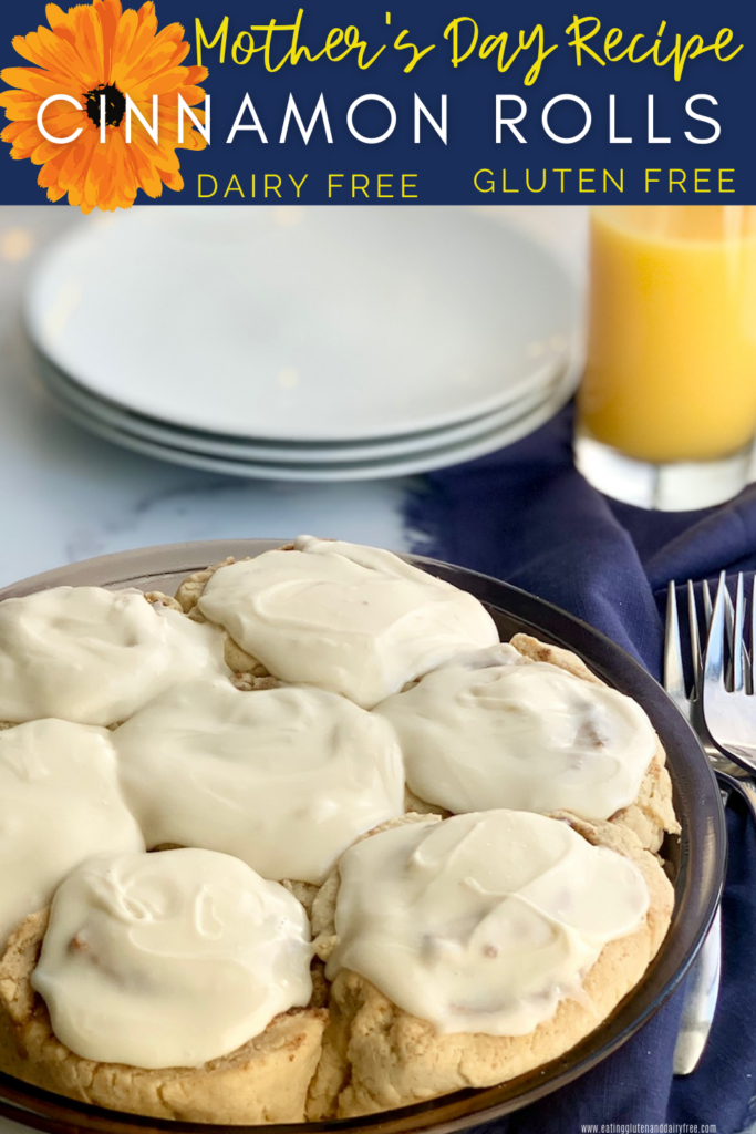 A pie plate filled with soft, gooey cinnamon rolls and topped with a decadent creamy dairy free cream cheese frosting next to serving plates and glass of orange juice.