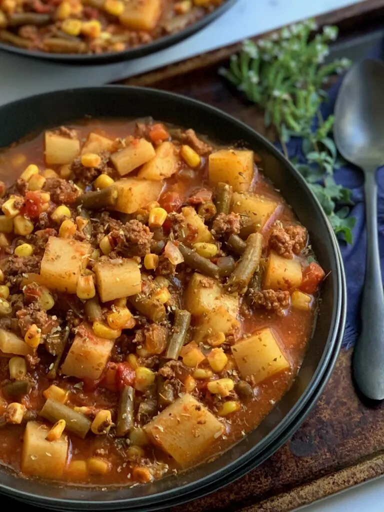 A black bowl full of hearty ground beef, potato chunks, fire roasted tomatoes, and veggies.