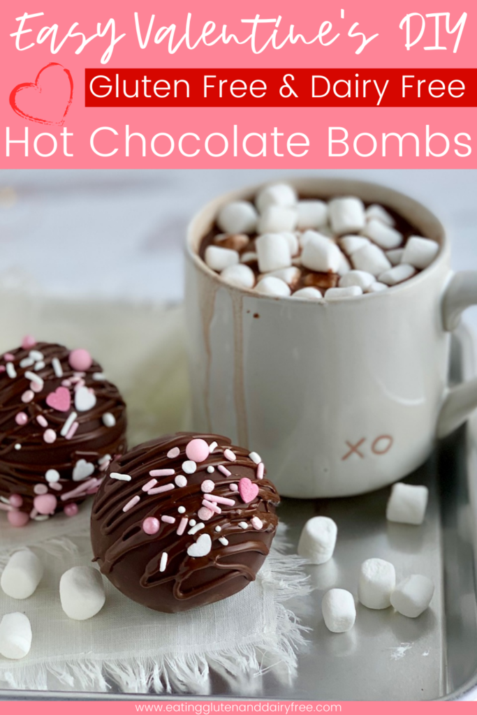 A hollow chocolate ball filled with hot chocolate mix and mini marshmallows. The outside of the ball has melted chocolate drizzle with white and pink sprinkles next to a mug of hot chocolate.