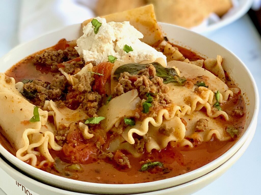 A bowl full of lasagna noodles, ground beef, Italian sausage, and tomato base topped with dairy free ricotta.