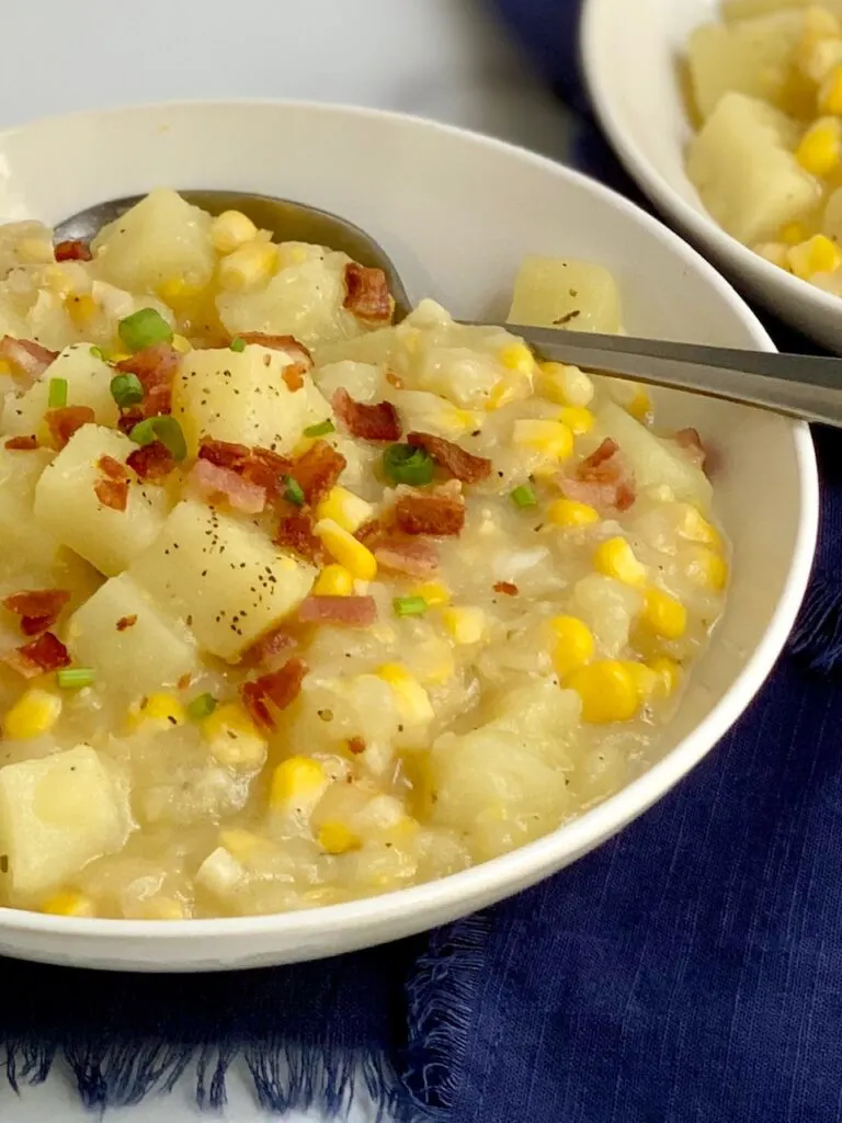 A soup bowl filled with potato corn chowder-- tender potato chunks, sweet corn topped with bacon pieces.