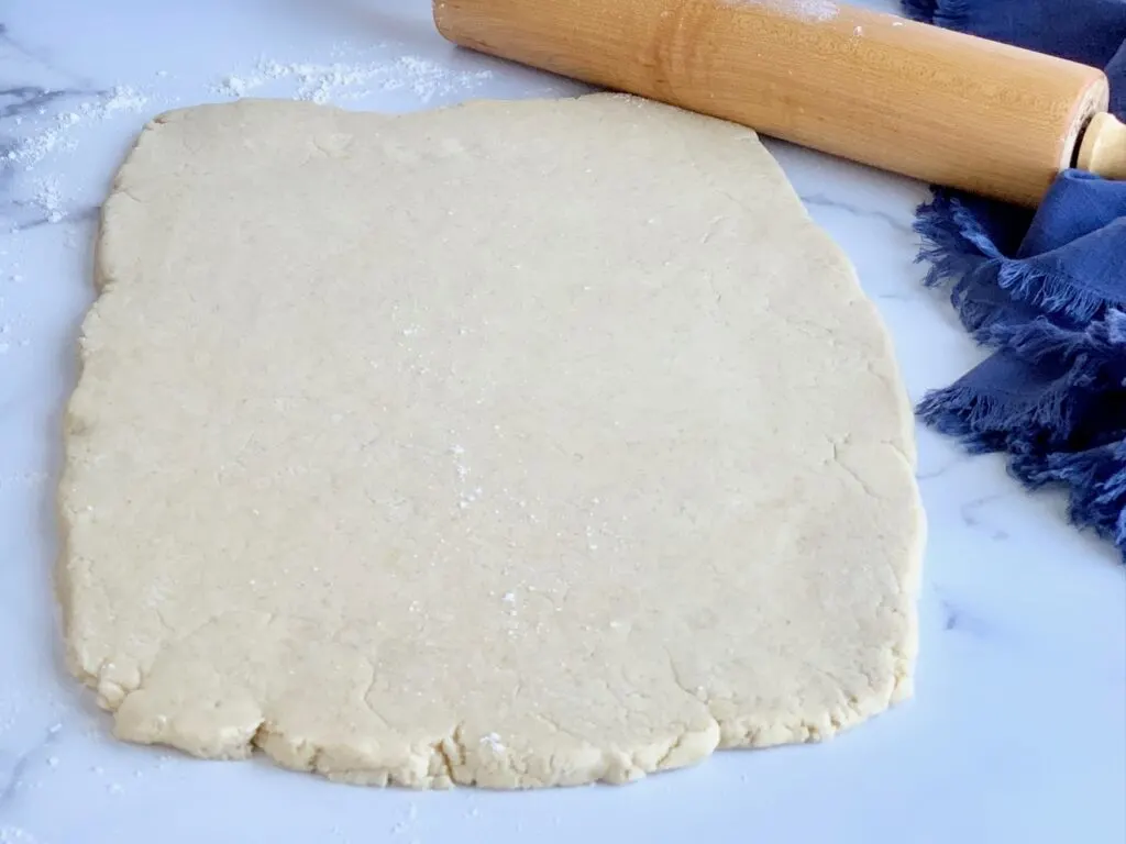 Rectangle shaped dough rolled out next to a rolling pin.