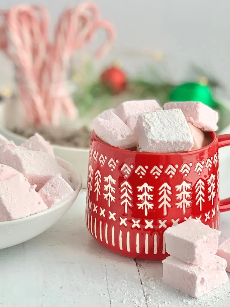 A red Christmas mug filled with hot chocolate and topped with fluffy pink peppermint marshmallows.