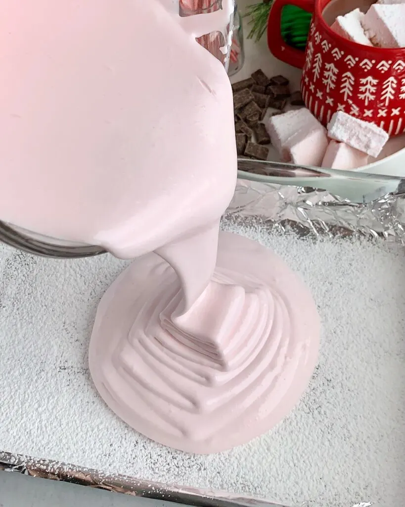 Pouring the thickened marshmallow mixture into the prepared 9 x 13 in baking pan with cornstarch and powdered sugar.