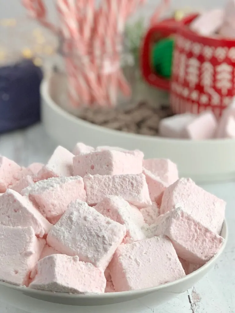 A white bowl full of square, fluffy pink homemade marshmallows.