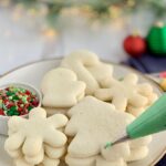 A large plate of Christmas sugar cookies next to a bag of green icing