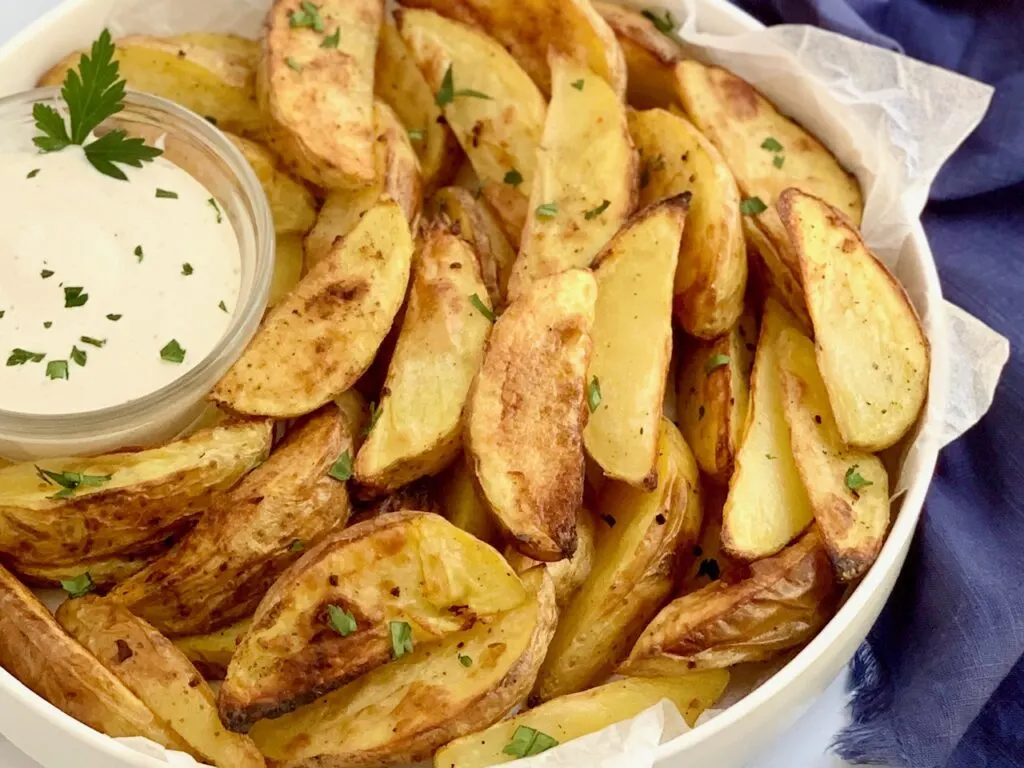 A large serving plate of baked potato wedges with dipping sauce. 