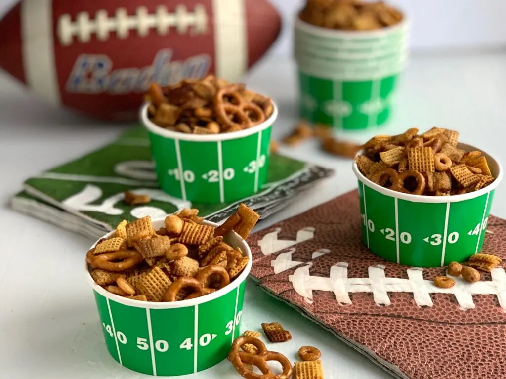 Mini football bowl filled with handfuls of Chex mix-- peanuts, pretzels, and two types of Chex mix. 