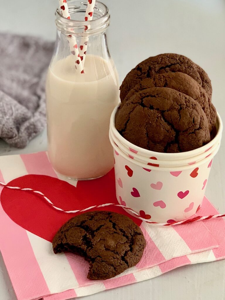 Round brownie cookies with a bite eaten out of one next to a glass of dairy free milk.
