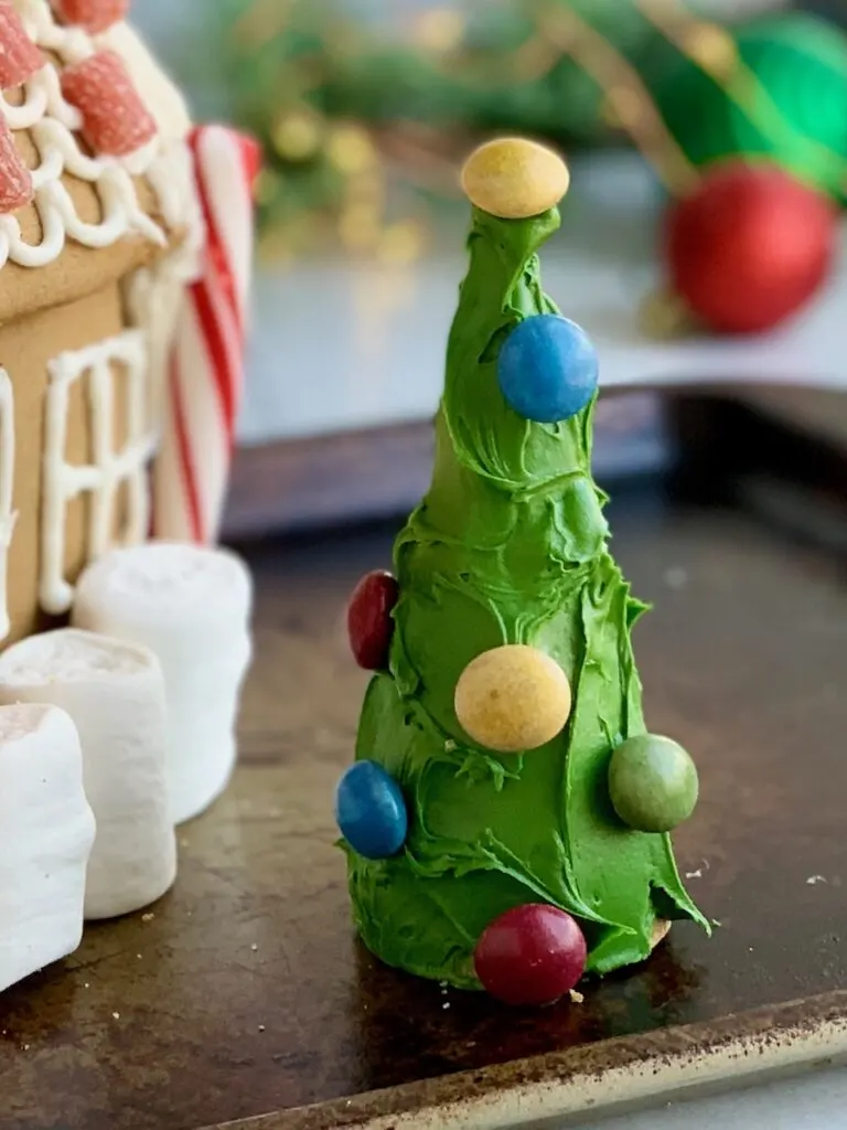 An upside down ice cream cone decorated as a tree with green frosting and colorful candies on it.