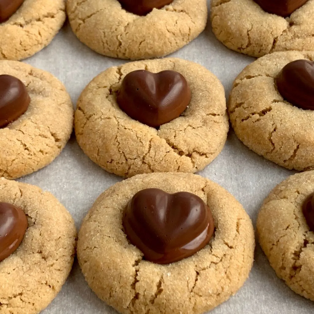 Several round peanut butter cookies with a chocolate heart pushed down in the middle.