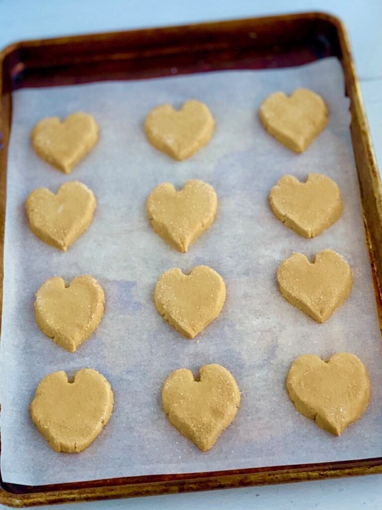 A baking sheet full of raw peanut butter cookies in the shape of a heart.