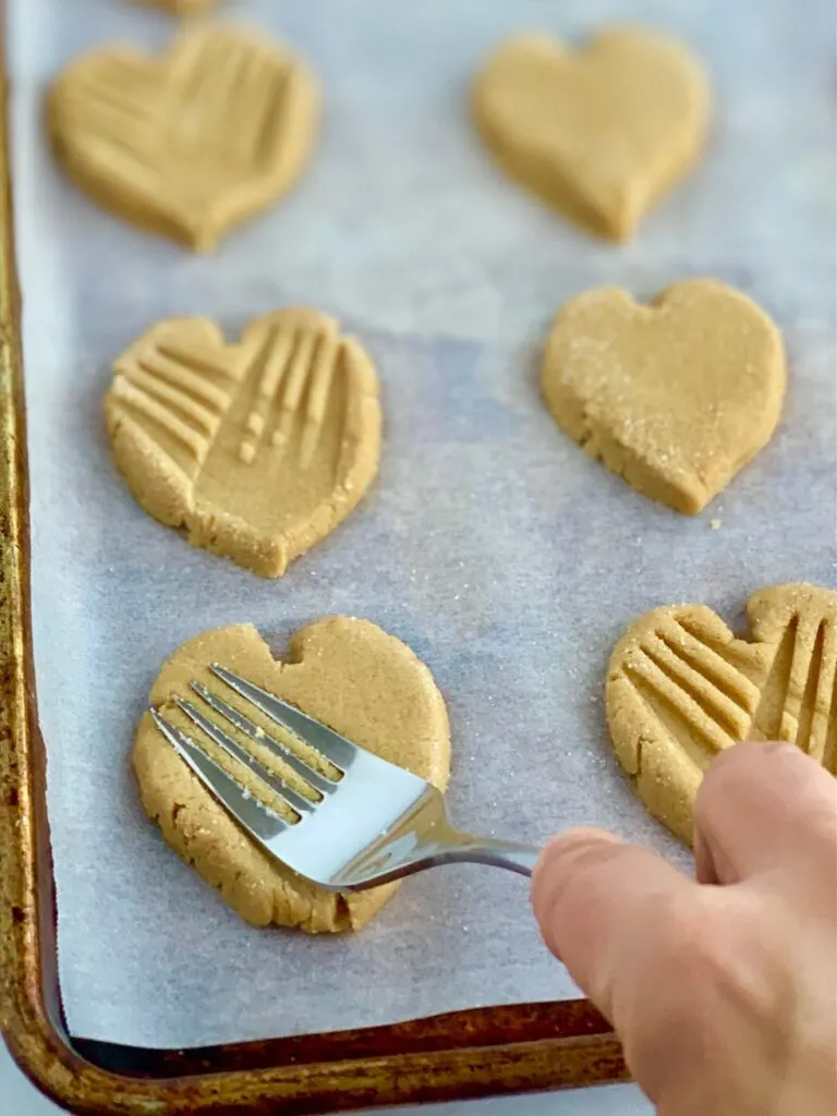 A fork making crisscross patterns in a heart-shaped cookie.