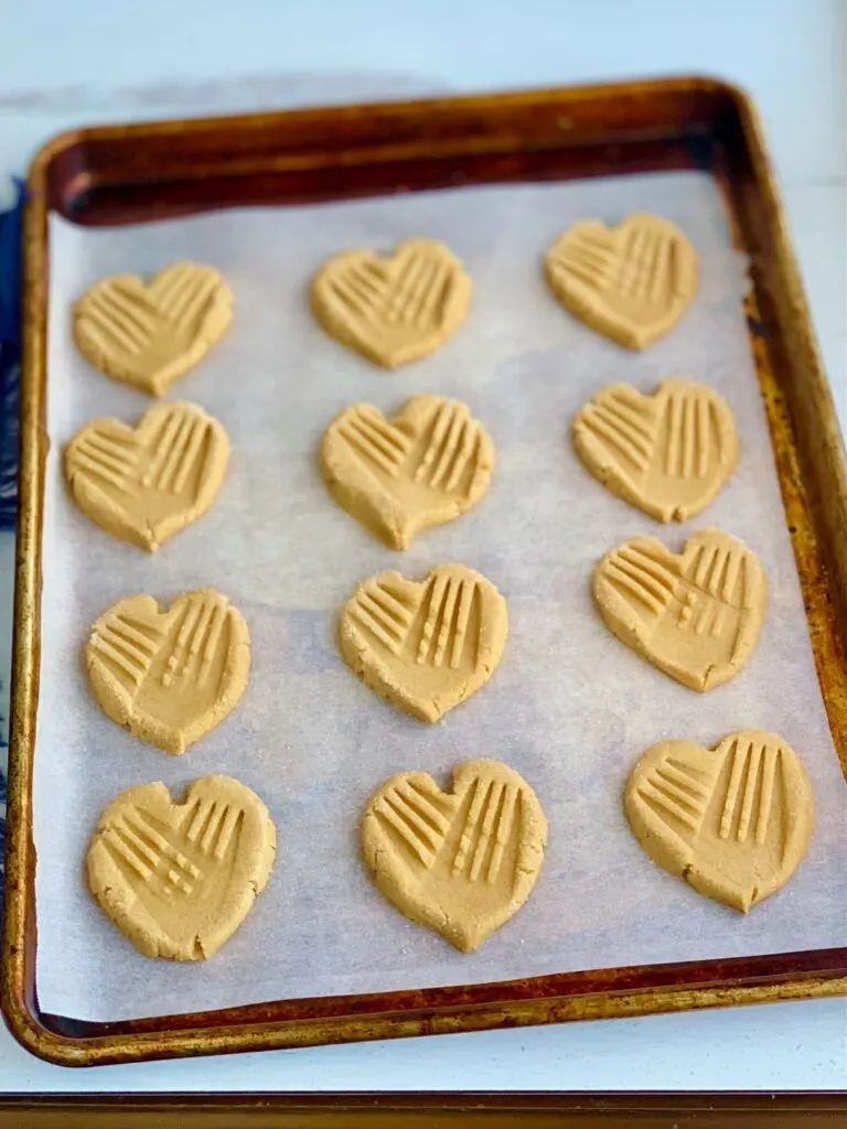 A baking sheet full of heart-shaped cookies with traditional crisscross marks on them.