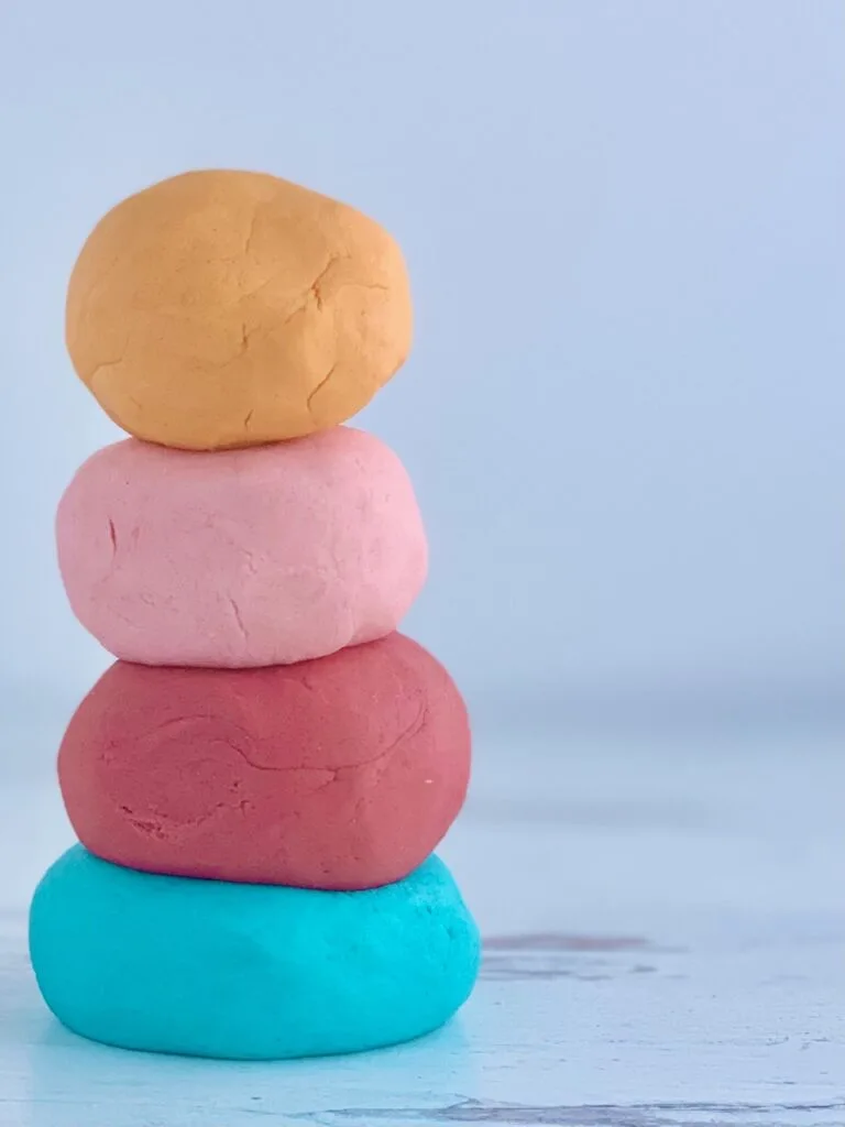 4 balls of playdough stacked on top of each other, blue, dark pink, light pink, and orange.