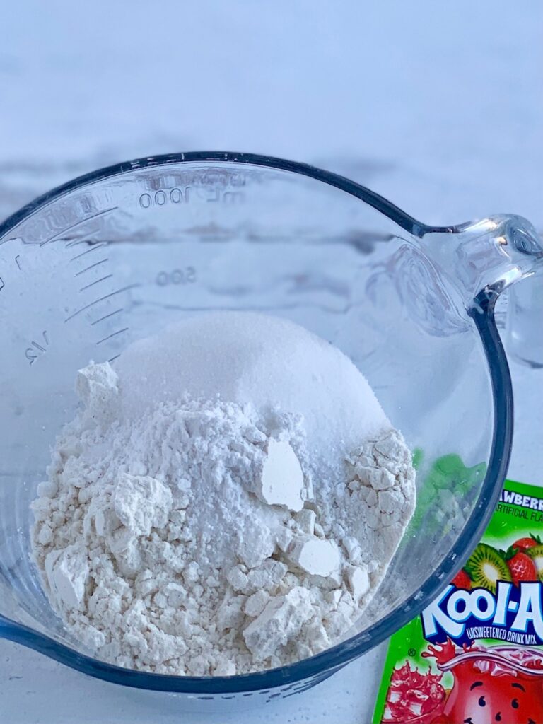 A glass mixing bowl with flour, salt, and cream of tarter in it.