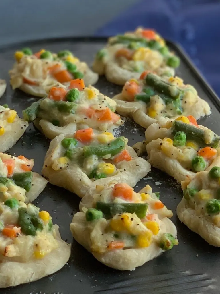 Mini chicken pot pies in a 12 compartment mini muffin pan. Each pot pie is filled with corn, green beans, carrots, and peas. 