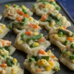 Mini muffin pan filled with a dough crust and shredded chicken and veggie filling.