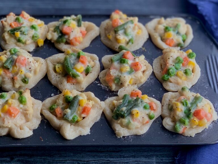 A mini muffin pan filled with a buttery baked crusts in each compartment and then topped with a shredded chicken and veggie filling.