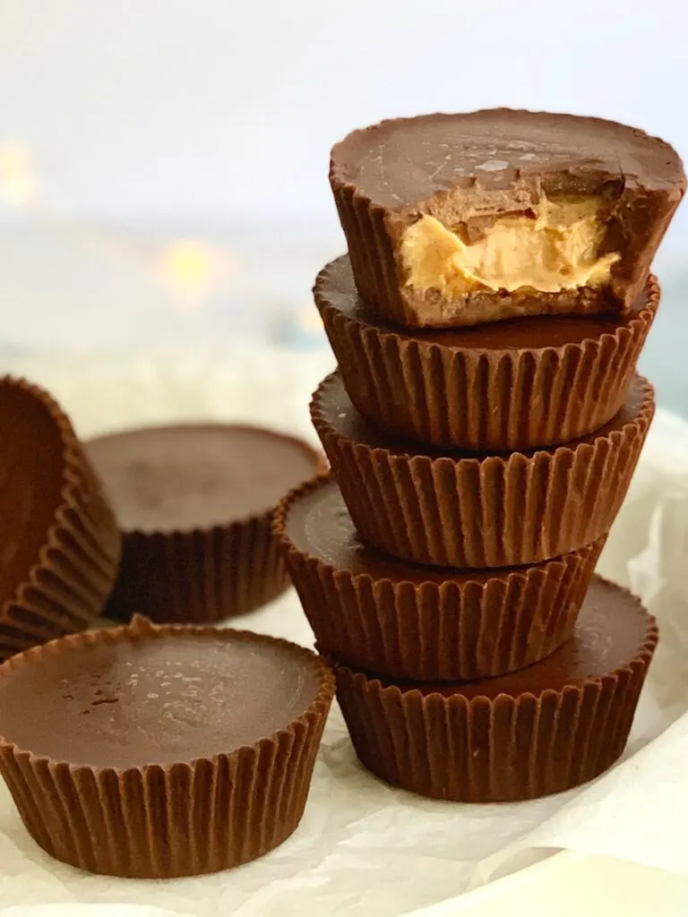 a plate of stacked peanut butter cups and a bite missing out of the top cup. You can see peanut butter. 