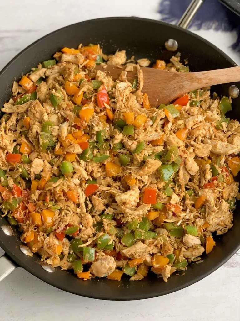 A skillet heaping with shredded chicken, onions, bell peppers, and seasonings. 