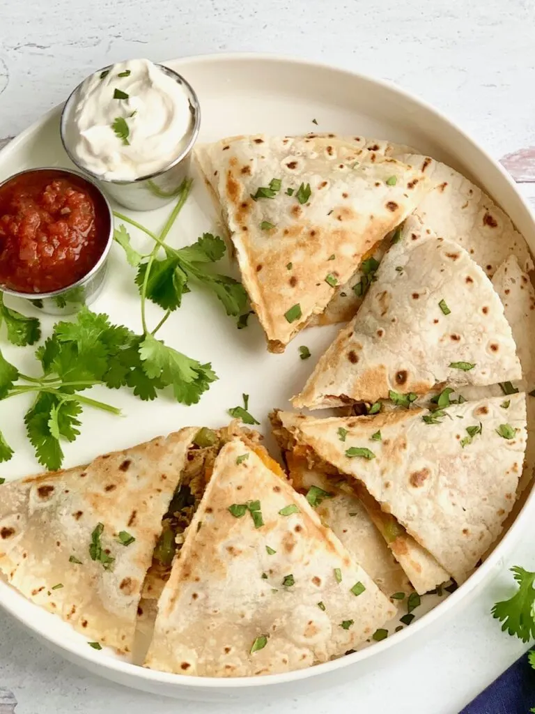 A serving plate of quesadillas cut into triangles and ready to be eaten with a side of dairy free sour cream and salsa.