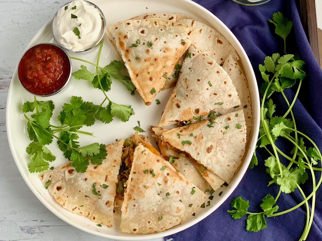 A serving plate of quesadillas cut into triangles and ready to be eaten with a side of dairy free sour cream and salsa.