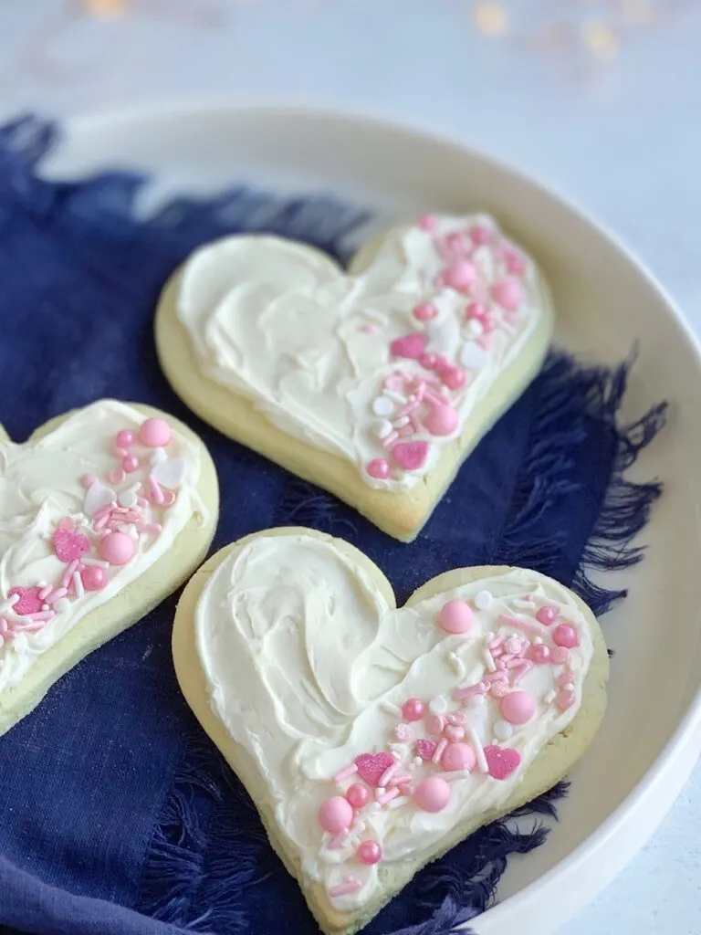 3 heart shaped sugar cookies with white frosting and pink and white sprinkles on the right side of each cookie.