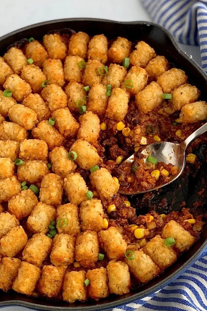 A skillet filled with ground beef, corn, black beans, and taco spices topped with tater tots out of the oven.