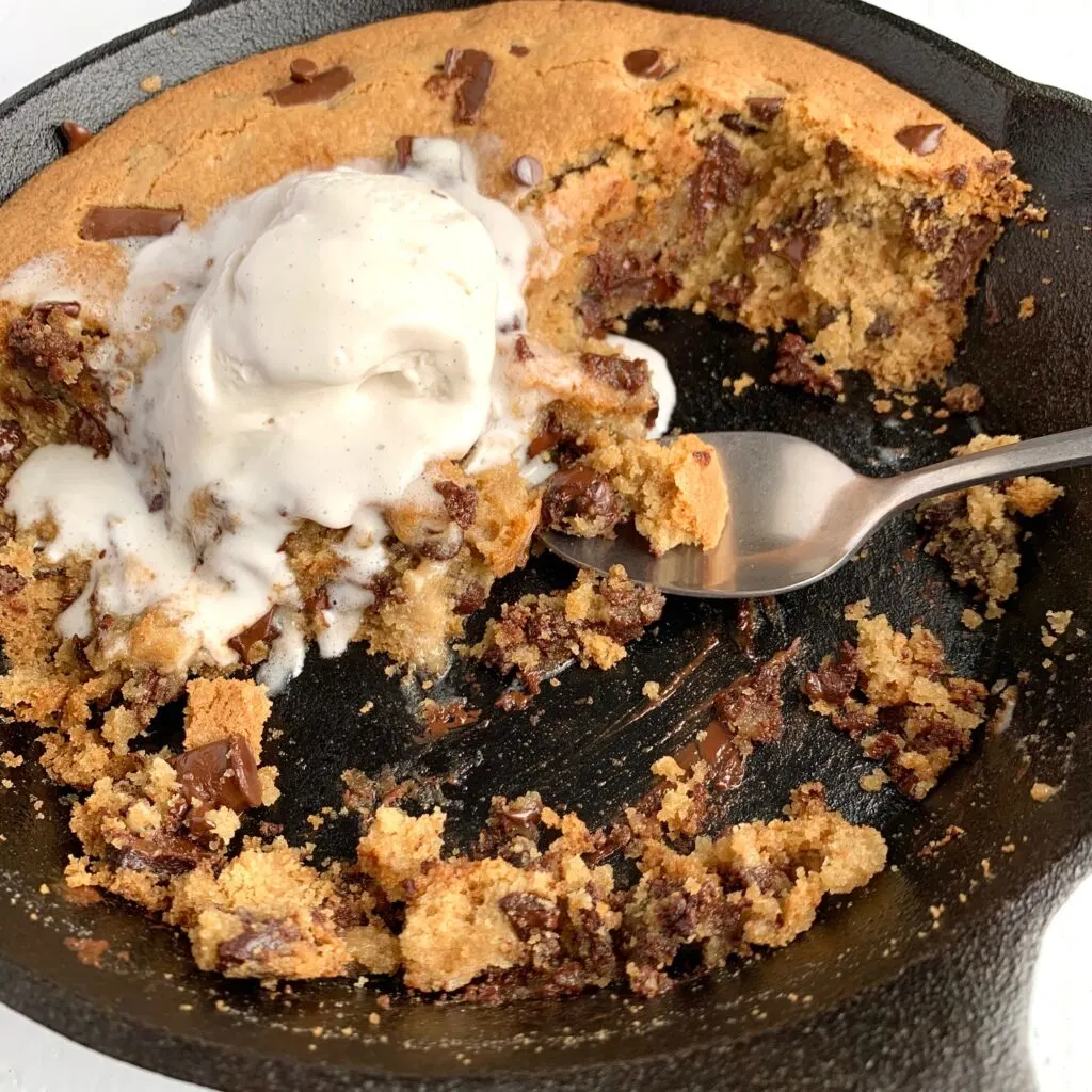 A cast inro skillet filled with a giant baked chocolate chip cookie topped with ice cream.