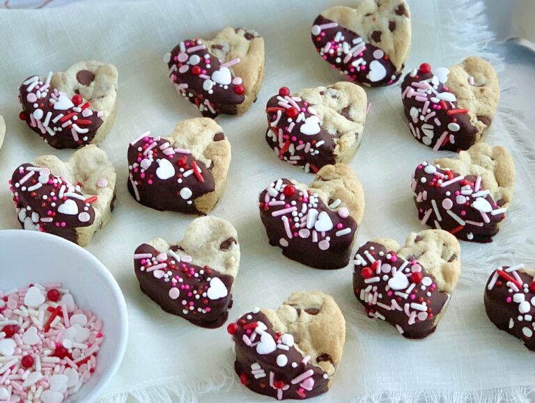 Rows of heart-shaped chocolate chip cookies dipped in chocolate with sprinkles on top