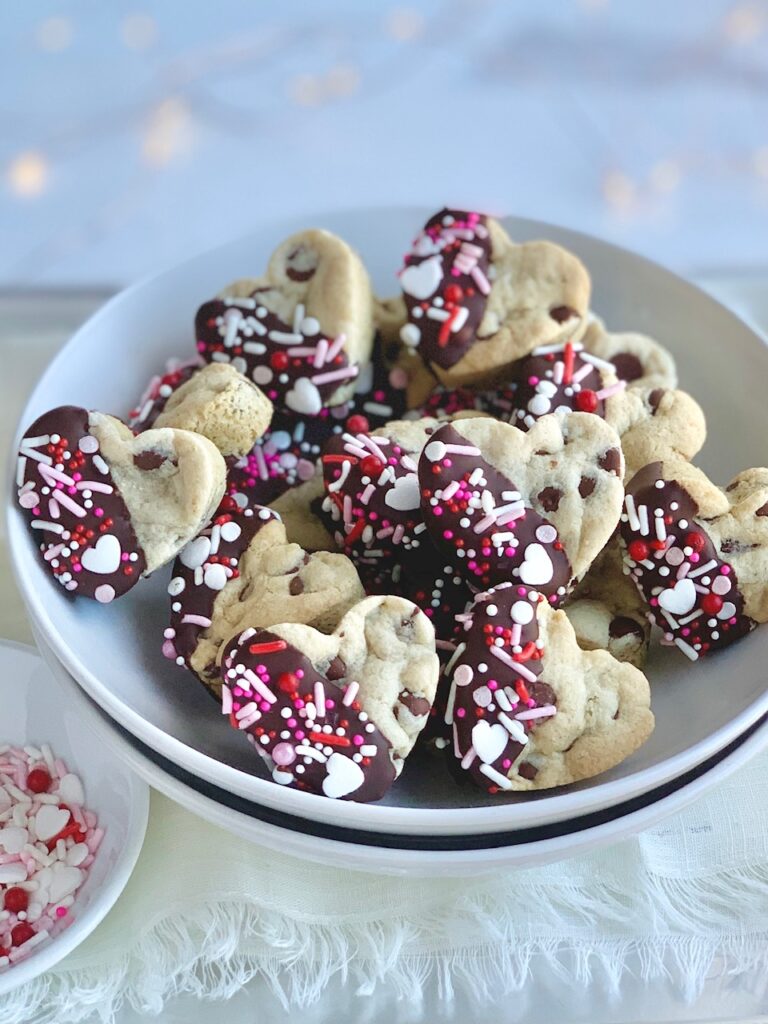 A bowl of heart-shaped chocolate chip cookies that have been dipped in chocolate and topped with sprinkles. 
