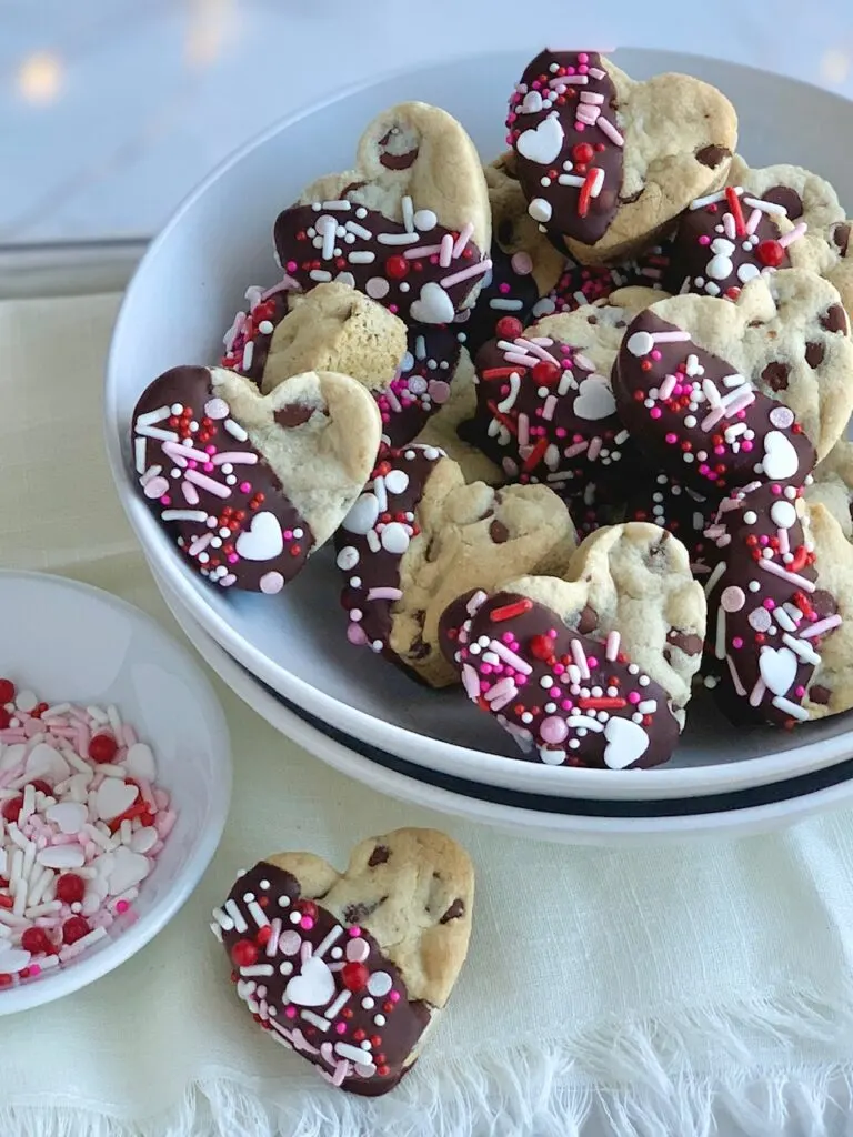 A bowl of heart-shaped chocolate chip cookies that have been dipped in chocolate and topped with sprinkles. 