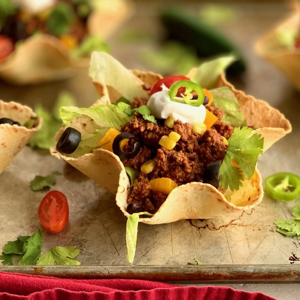 A tortilla made into a beautiful taco shell shape with ground meat, corn, lettuce, and a dollop of dairy free sour cream.