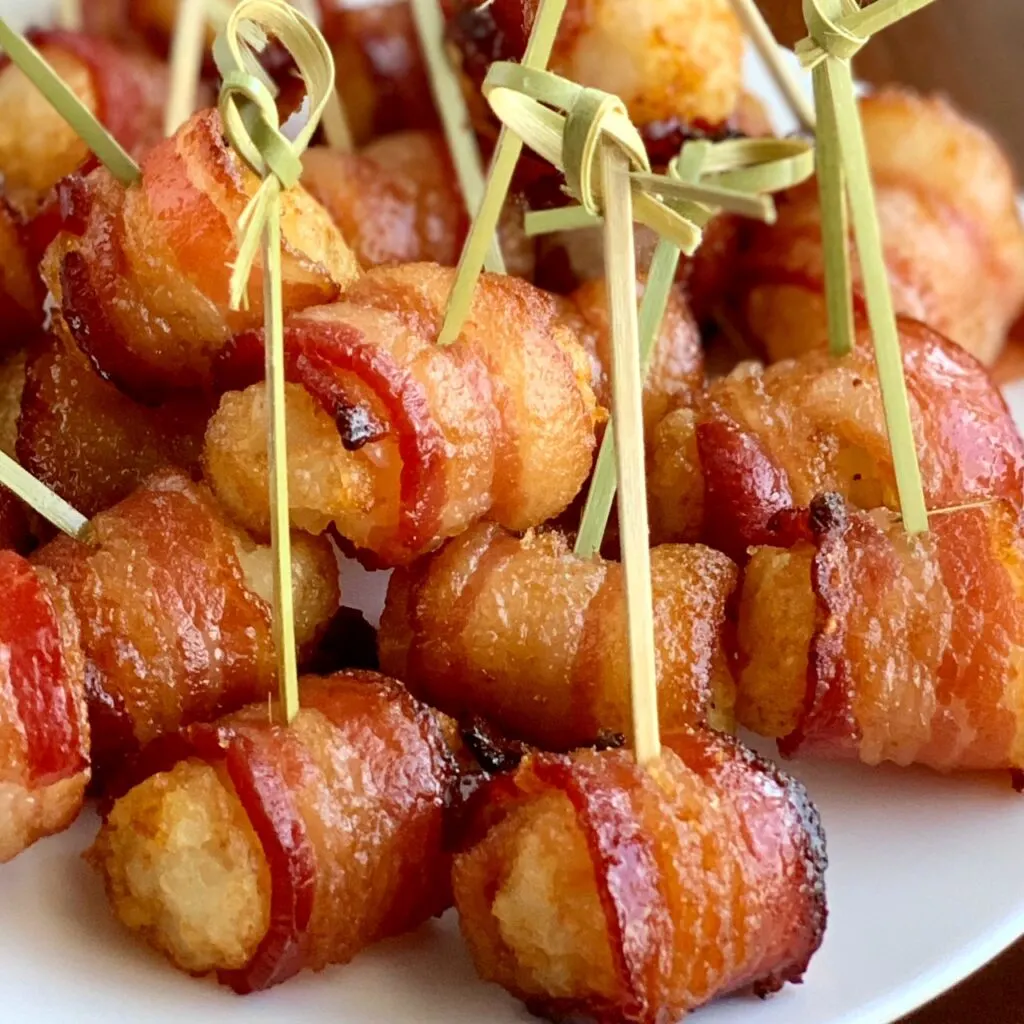 A plate full of individual tater tots wrapped in a slice of bacon.