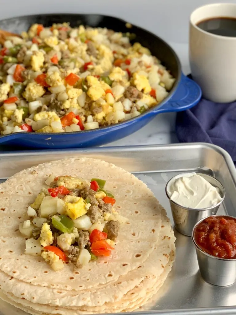 A breakfast burrito mixture on top of several soft tortillas next to dairy free cream cheese ad salsa.