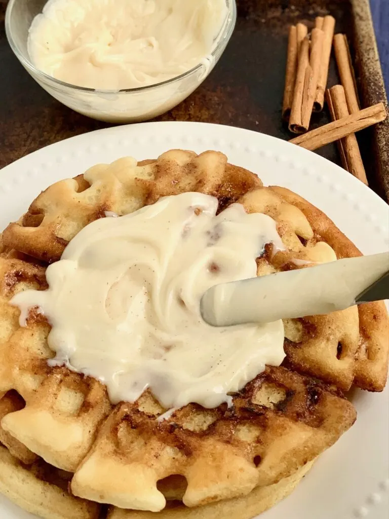 A waffle with a cinnamon swirl in it and a cream cheese frosting on top of it.