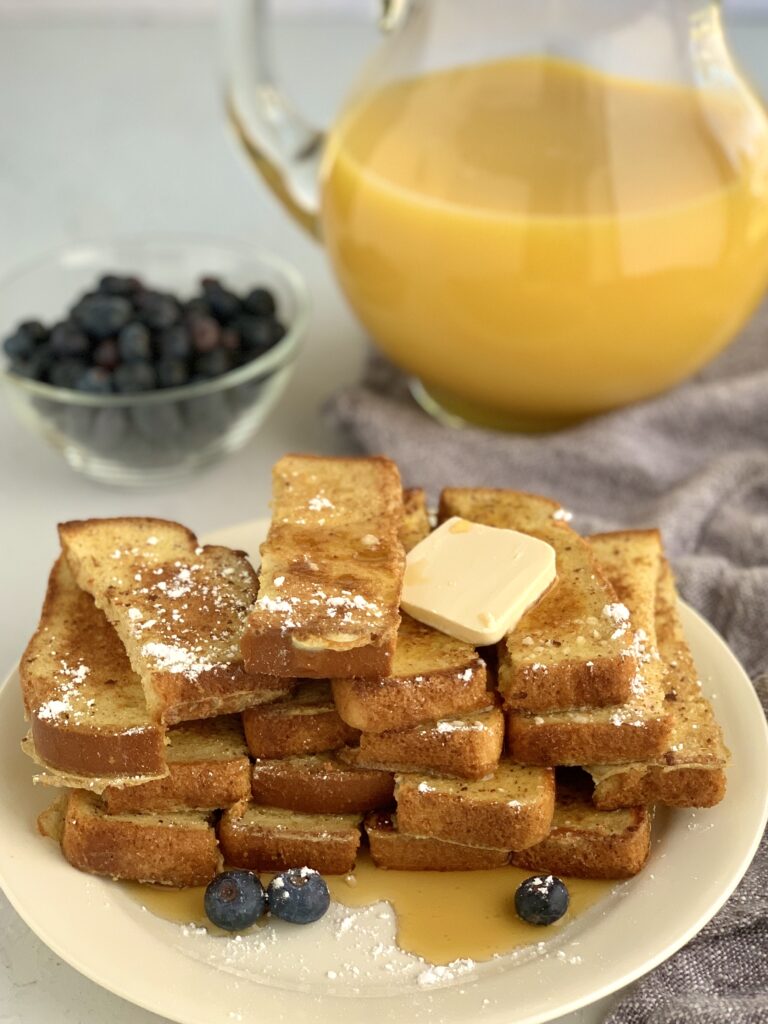 A plate of French Toast sticks with butter, syrup, and blueberries.