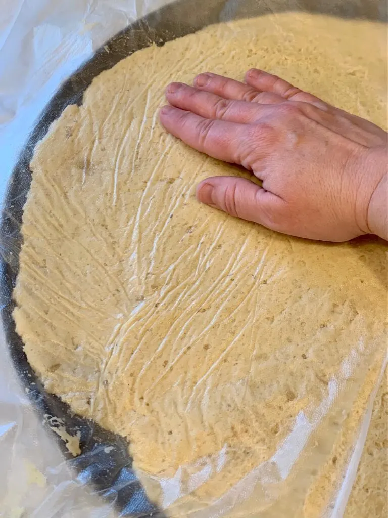 A hand pushing down raw pizza dough onto a pizza pan.