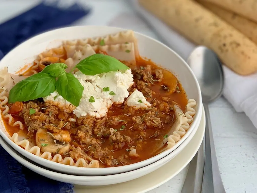 A large soup bowl filled with tender lasagna noodles, ground beef, Italian sausage, sliced mushroom's, and topped with creamy dairy free ricotta.