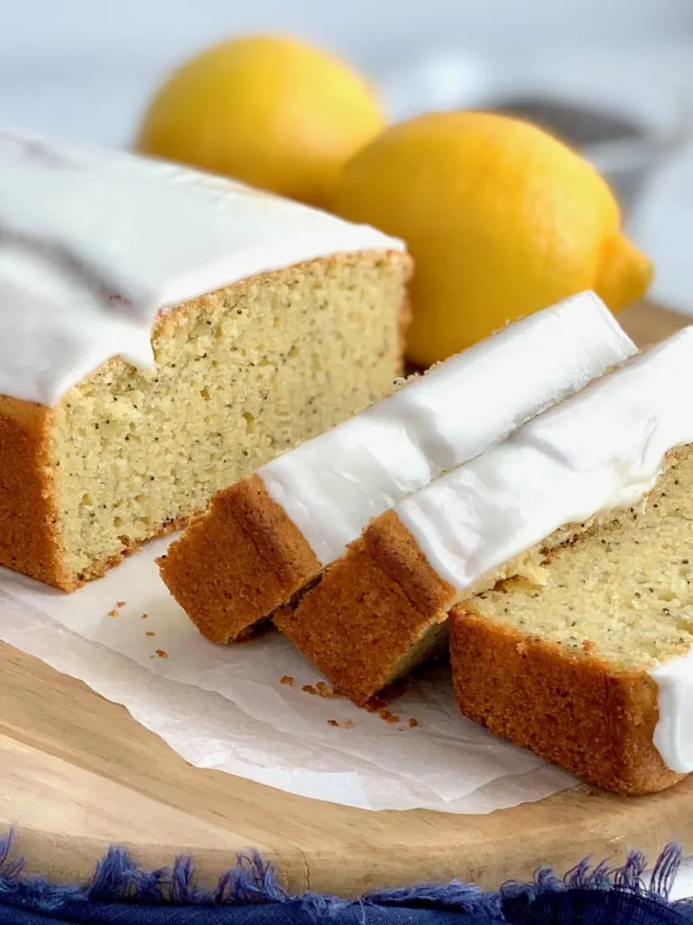 Slices of tender lemon poppy seed bread with a thick icing on top next to two whole lemons.