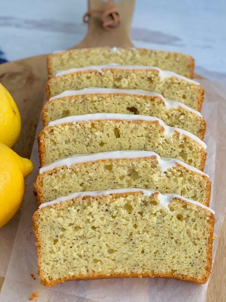 Slices of tender lemon poppy seed bread with a thick icing on top next to two whole lemons.