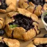 A rustic version of a blueberry pie. A flat crust with formed sides to hold a blueberry filling. On top is a fresh mint leave.